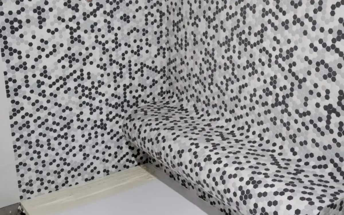 Banco curvo revestido con mosaico geométrico dentro de una ducha